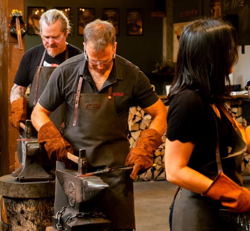 Participants shaping heated steel at anvils during a hands-on blacksmithing workshop.