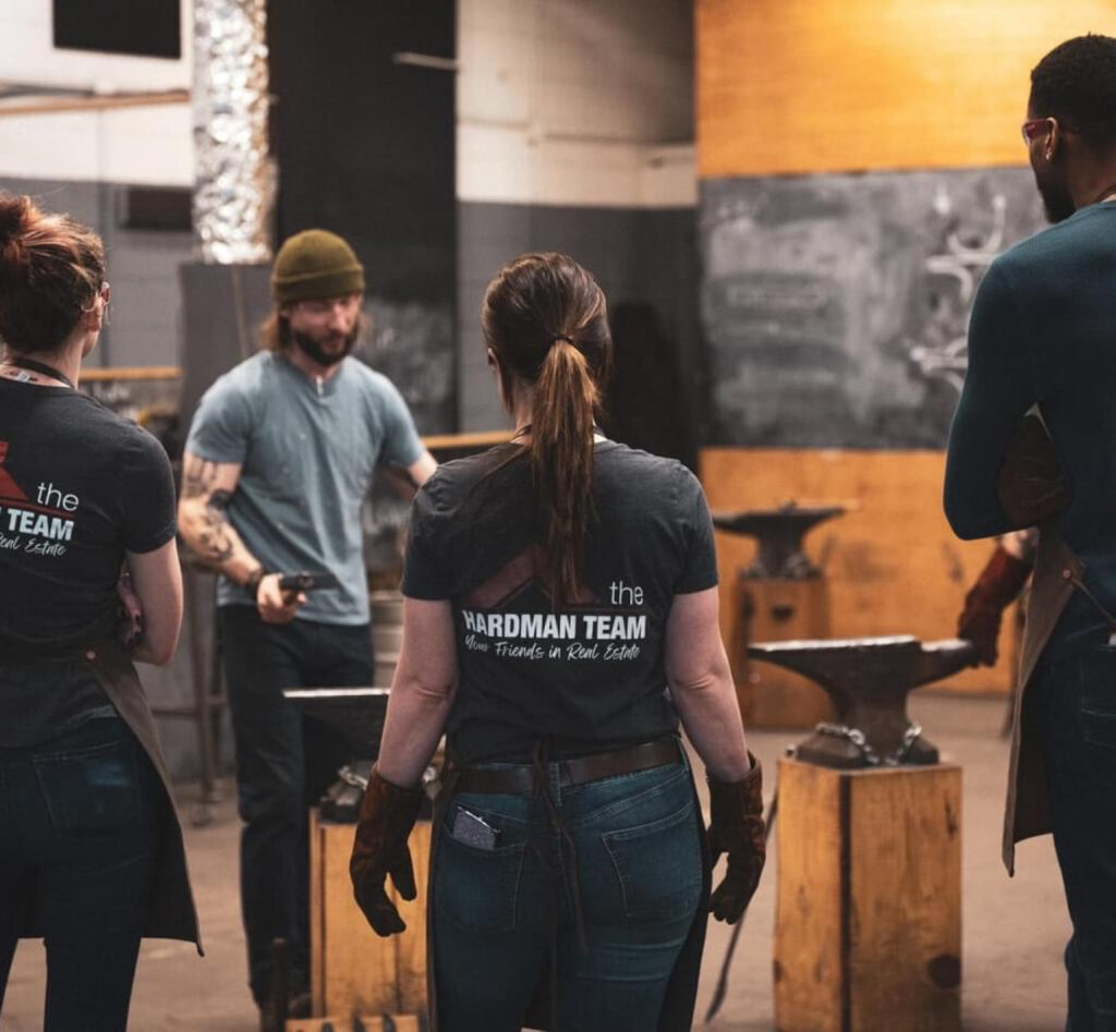 Private class workshop in action at Lawless Forge. Four people stand around anvils learning how to blacksmith